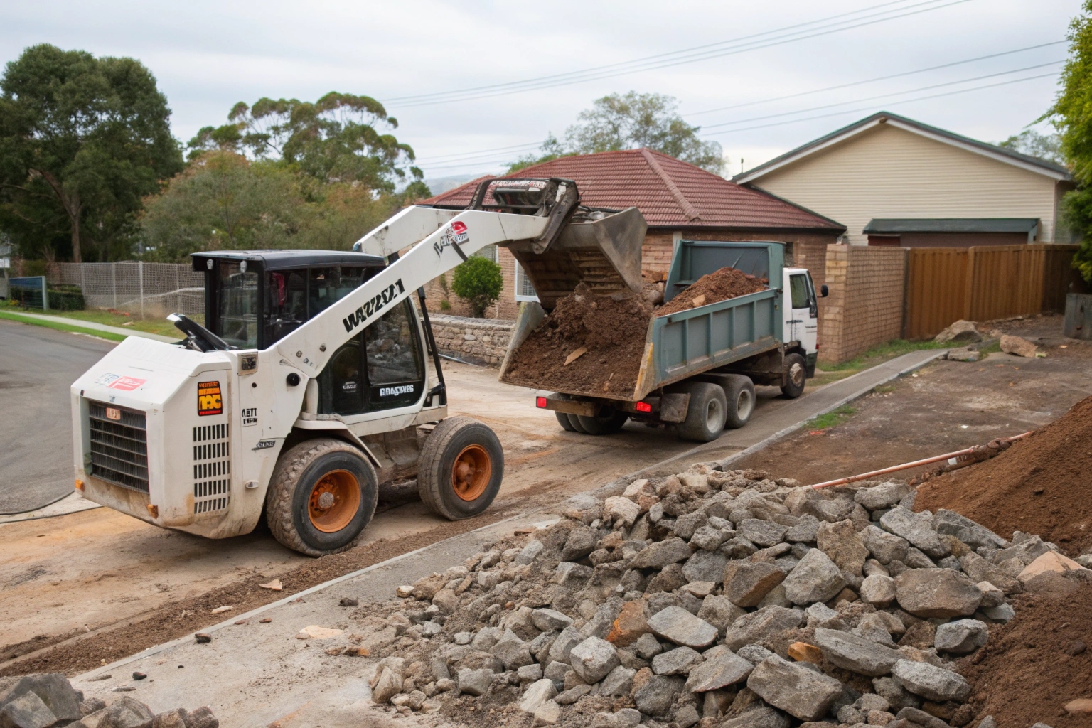 Bobcat loading broken concrete debris into tipper truck during residential demolition job